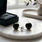 Close-up of black spherical resin stud earrings on a marble surface beside a black jewellery box, showing a sterling silver post and butterfly back.