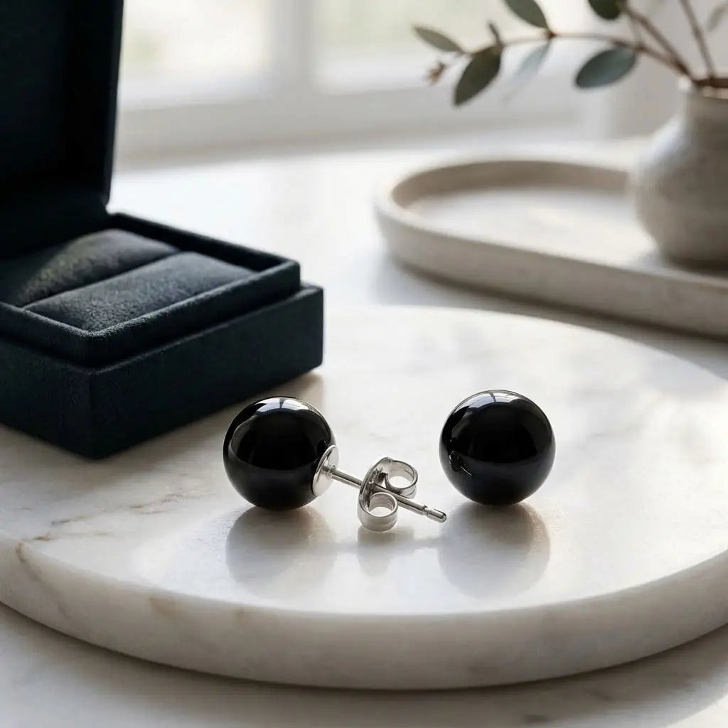 Close-up of black spherical resin stud earrings on a marble surface beside a black jewellery box, showing a sterling silver post and butterfly back.