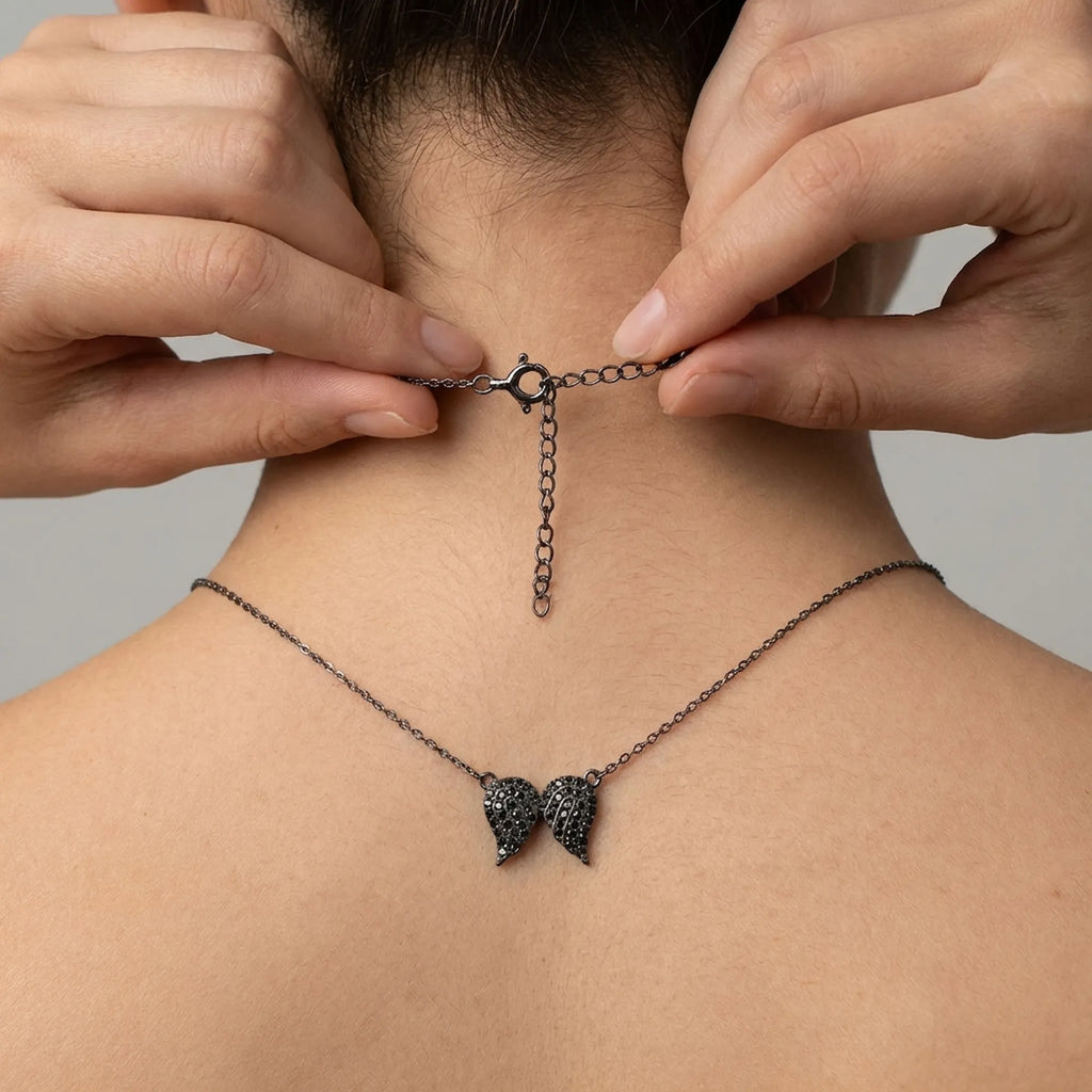 Hands seamlessly fastening the spring lock of the black rhodium plated pendant necklace, highlighting the 5cm extender chain fit.