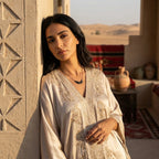 A woman in luxury MENA attire wearing the Black Zircon Wing Necklace against a desert architectural background.