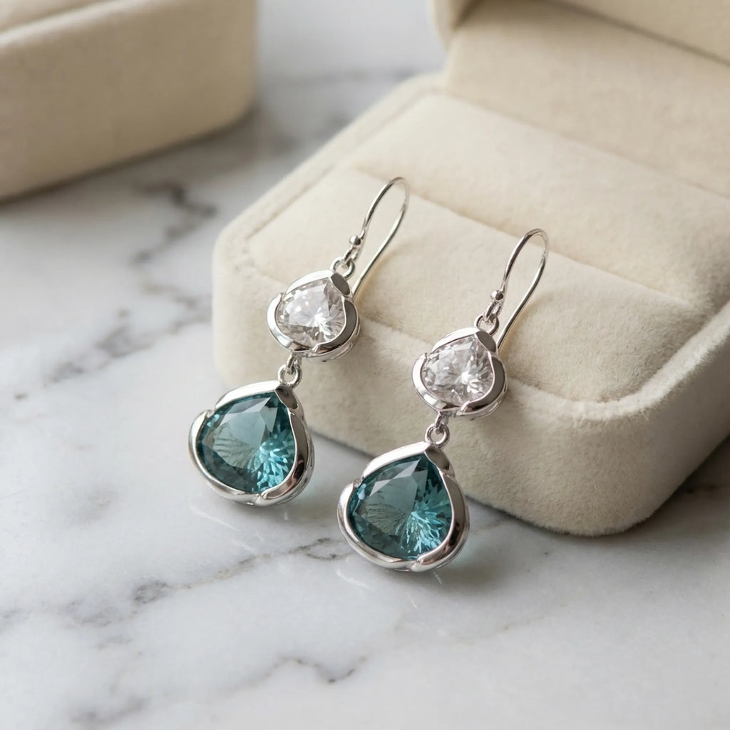 Blue and white topaz lotus silver earrings on a cream gift box, marble surface. Luna Dura.