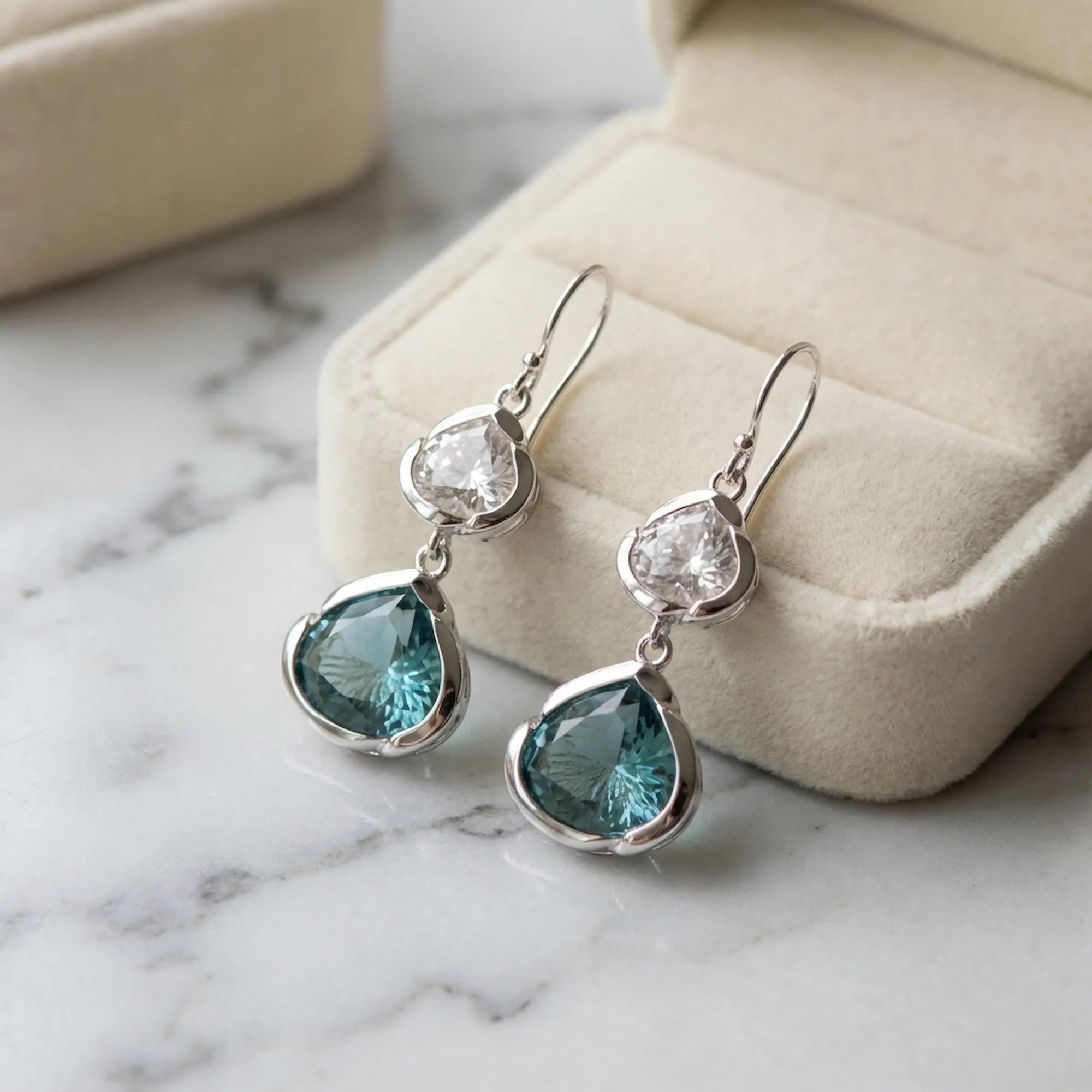 Blue and white topaz lotus silver earrings on a cream gift box, marble surface. Luna Dura.