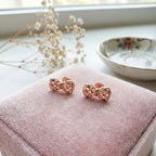 Rose gold woven bow stud earrings on pink velvet jewellery box with dried baby's breath