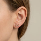 Rose gold woven bow stud earring on model with hair pulled back, neutral grey background