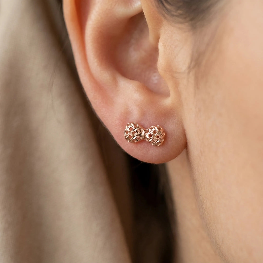 Close-up of rose gold woven bow stud earring worn on model earlobe, warm beige background Dubai 