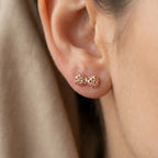 Close-up of rose gold woven bow stud earring worn on model earlobe, warm beige background Dubai 