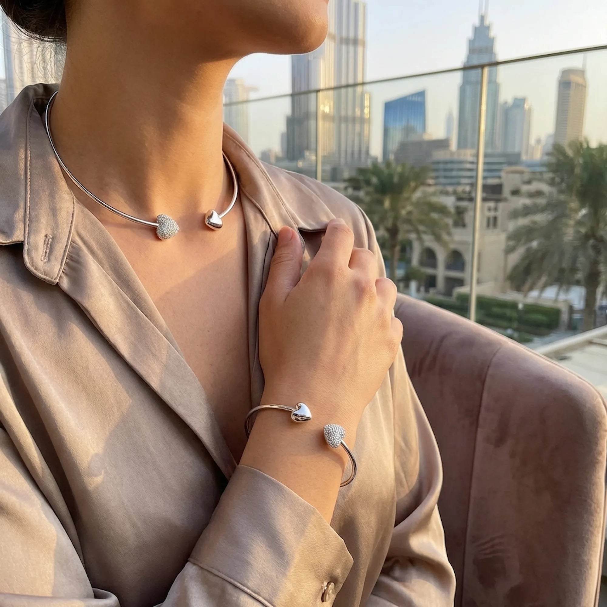 Sophisticated lifestyle shot of a woman wearing the cubic zirconia silver collar and matching bracelet while sitting outdoors with the Dubai skyline behind her.
