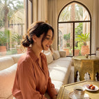 Stylish woman wearing the rose gold plume ear climbers while enjoying coffee in an elegant sunlit lounge in Dubai.