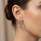 Two-tone silver and gold bypass hoop earring shown close on the ear — interlaced wave design in 925 sterling silver