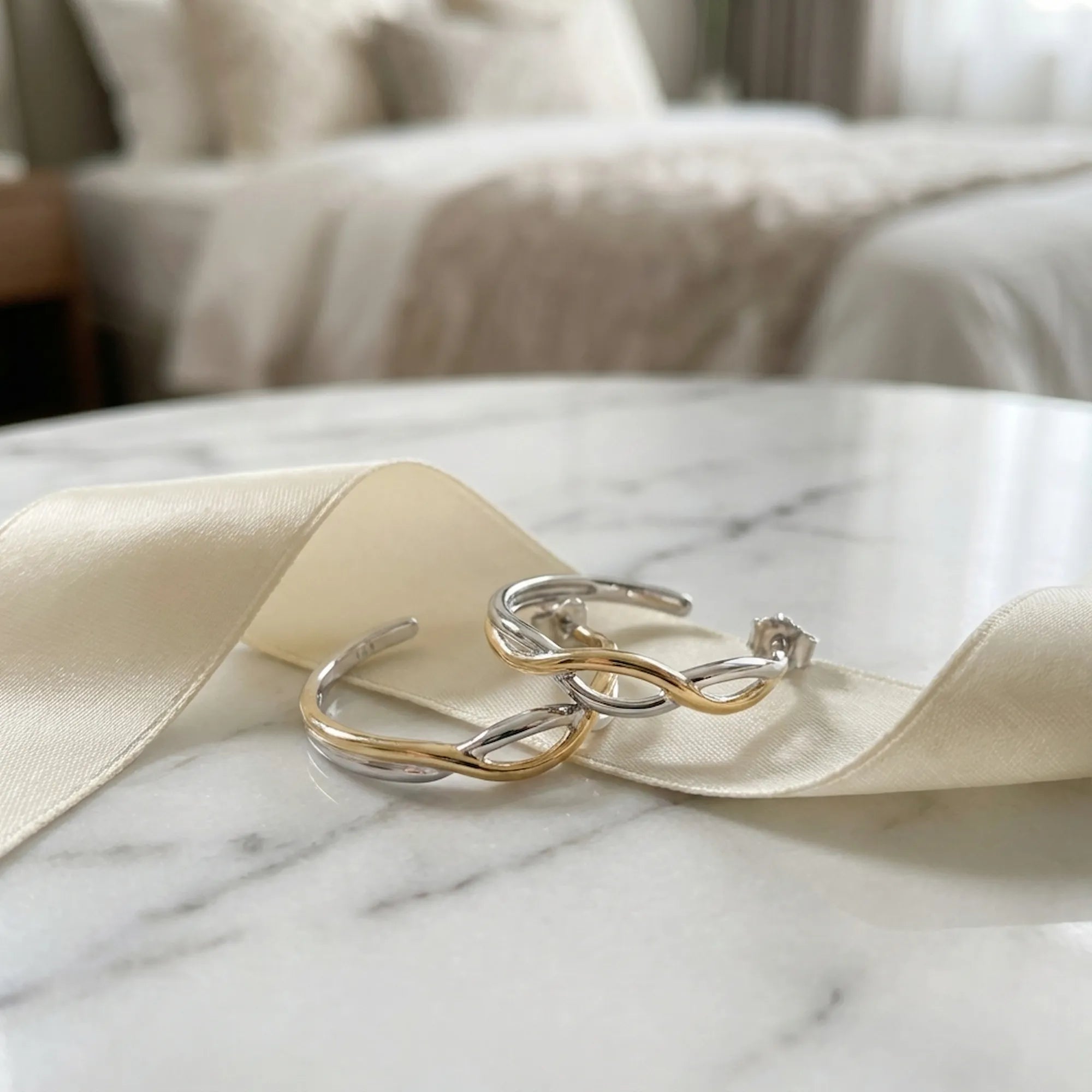 Two-tone silver and gold bypass hoop earrings on cream ribbon and marble — gift presentation in 925 sterling silver
