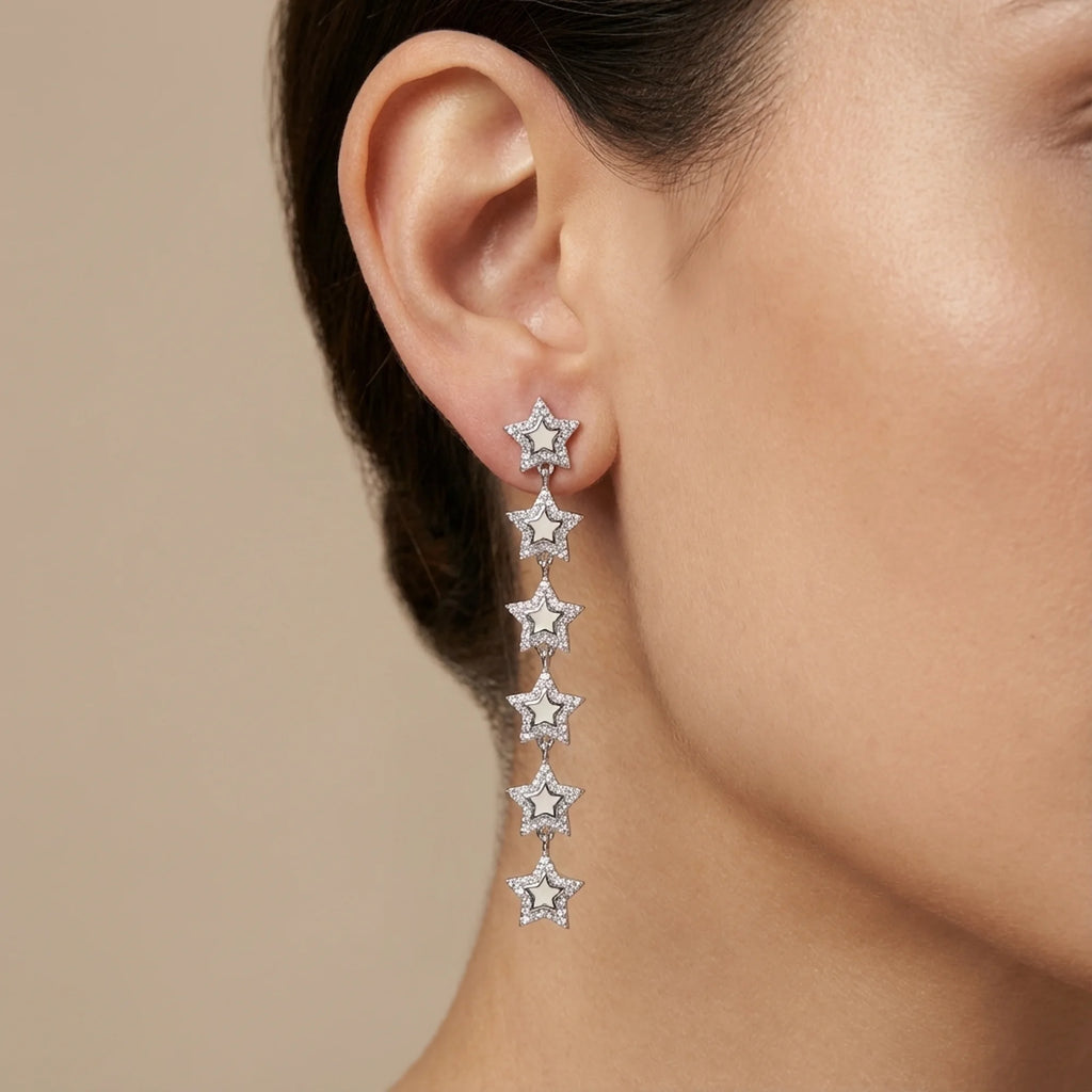 Woman wearing rhodium plated silver cascading star drop earrings with enamel outdoors in Dubai.