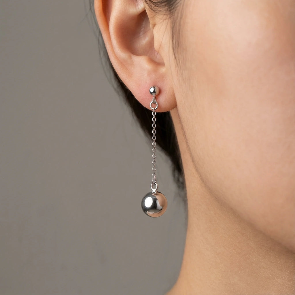 Woman wearing 925 sterling silver chain drop earrings with a polished 6mm sphere, outdoors in Dubai.