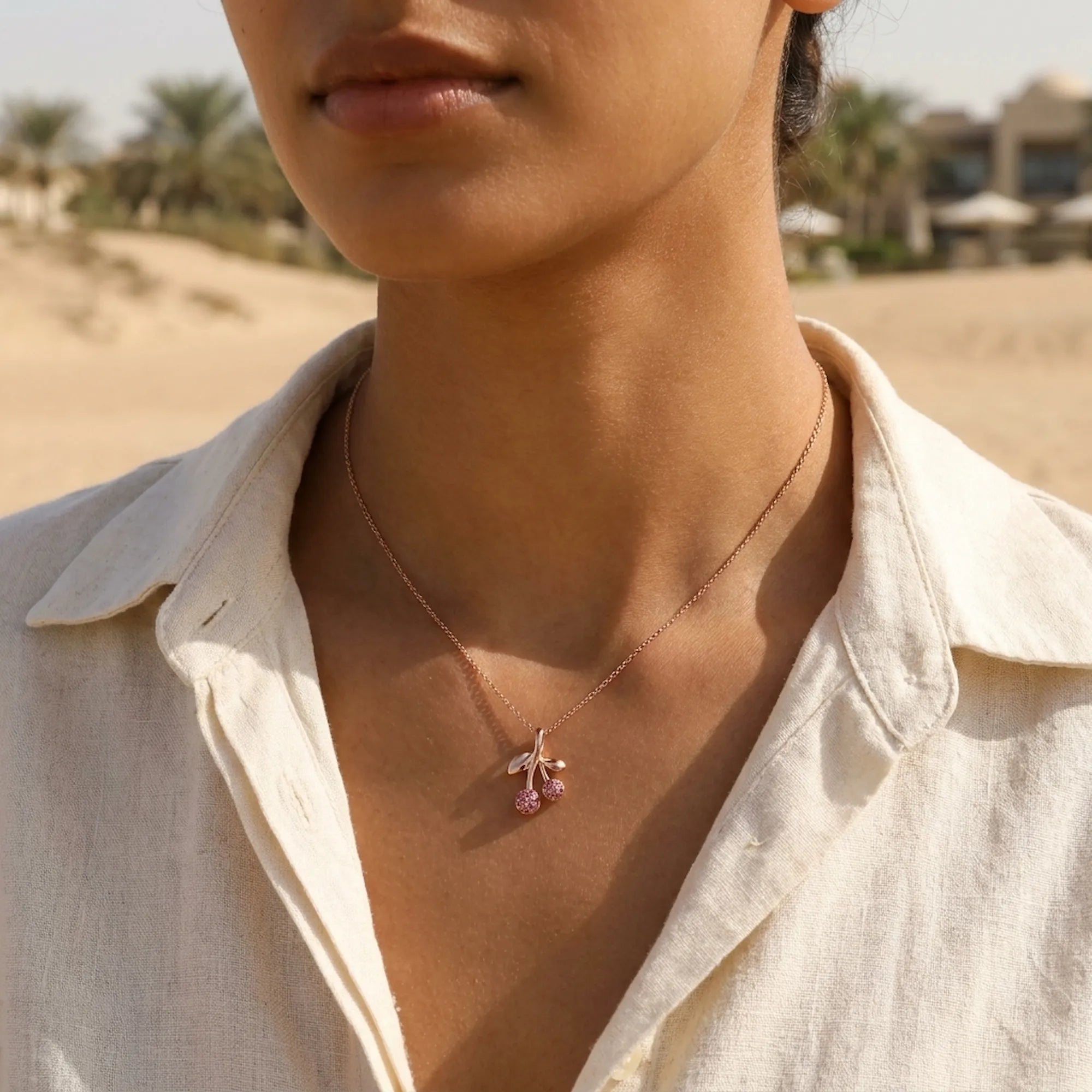 Cherry crystal pendant necklace worn at collarbone on model in linen top, Dubai desert landscape
