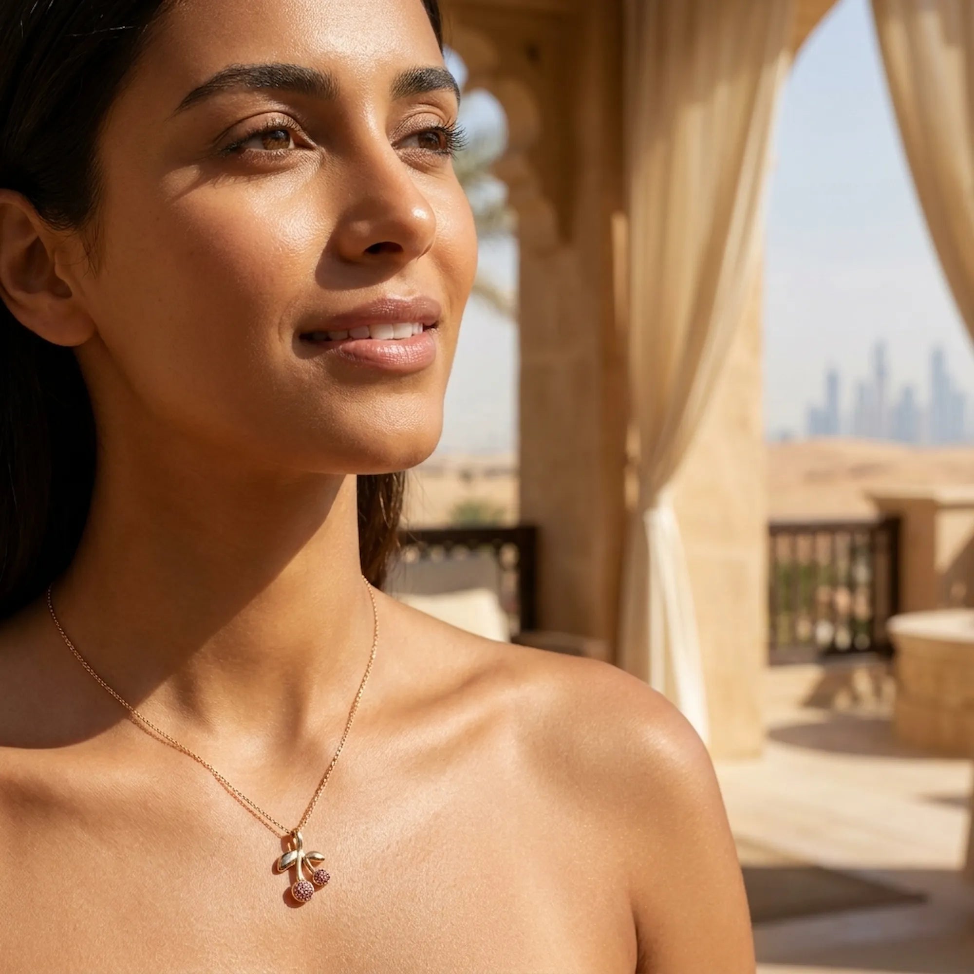 Rose crystal cherry pendant necklace on model at collarbone, Dubai heritage architecture and skyline in background