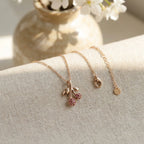 Cherry pavé pendant and 18K gold chain flat lay on linen — asymmetric rose crystals and extender chain detail