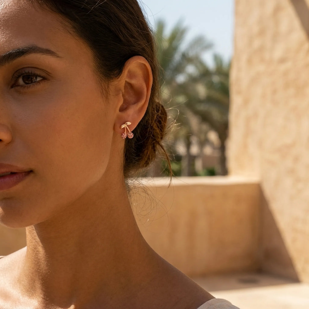 Double cherry crystal stud earring on model's ear with palm tree and Dubai arch architecture in background