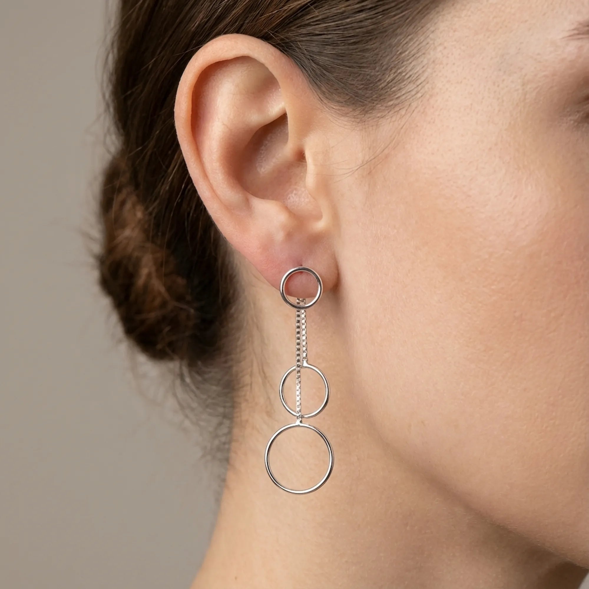 Close-up of ear wearing full silver circle cascade drop earring showing three descending open circles on box chain