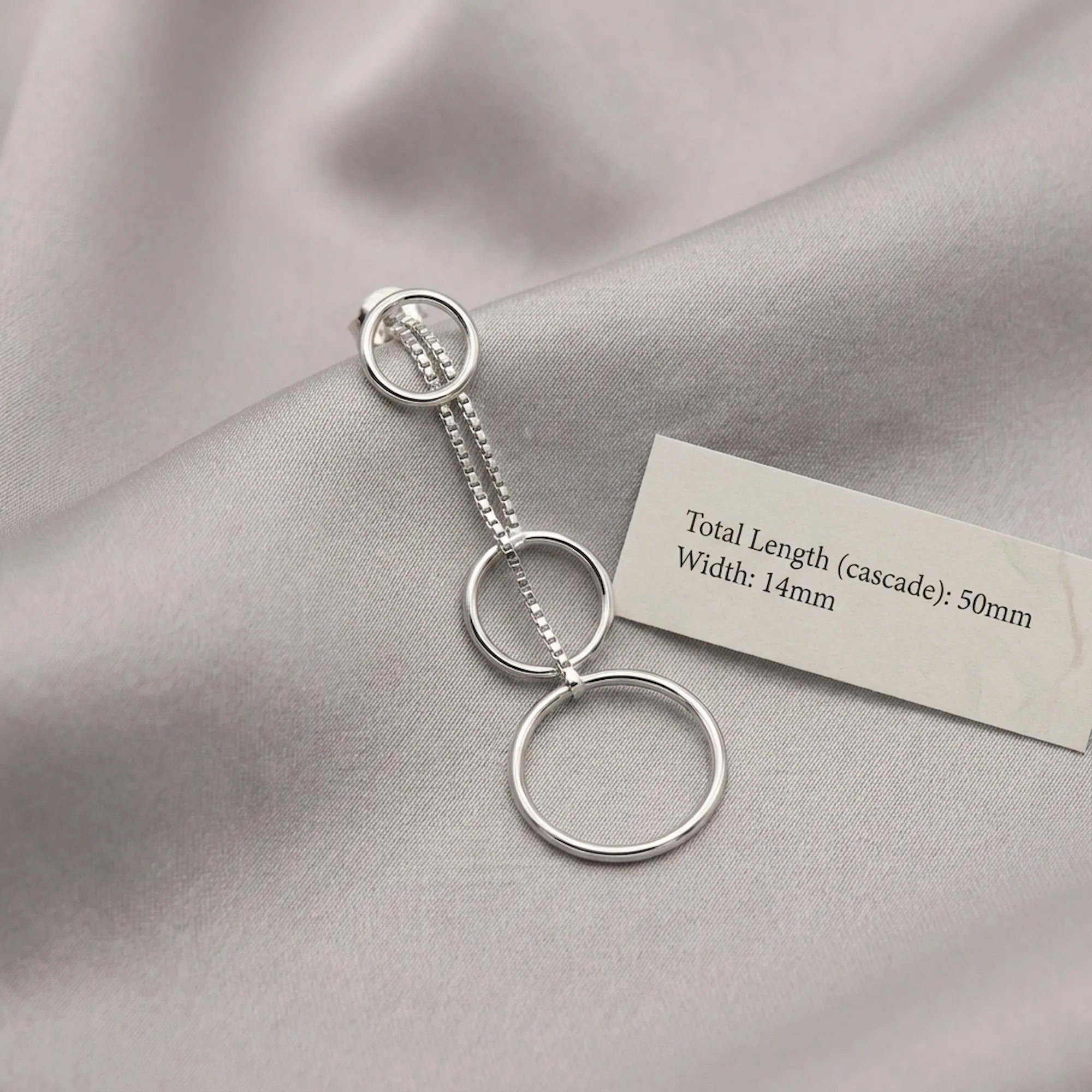 Silver circle cascade drop earring on grey fabric beside spec card showing 50mm total length and 14mm width