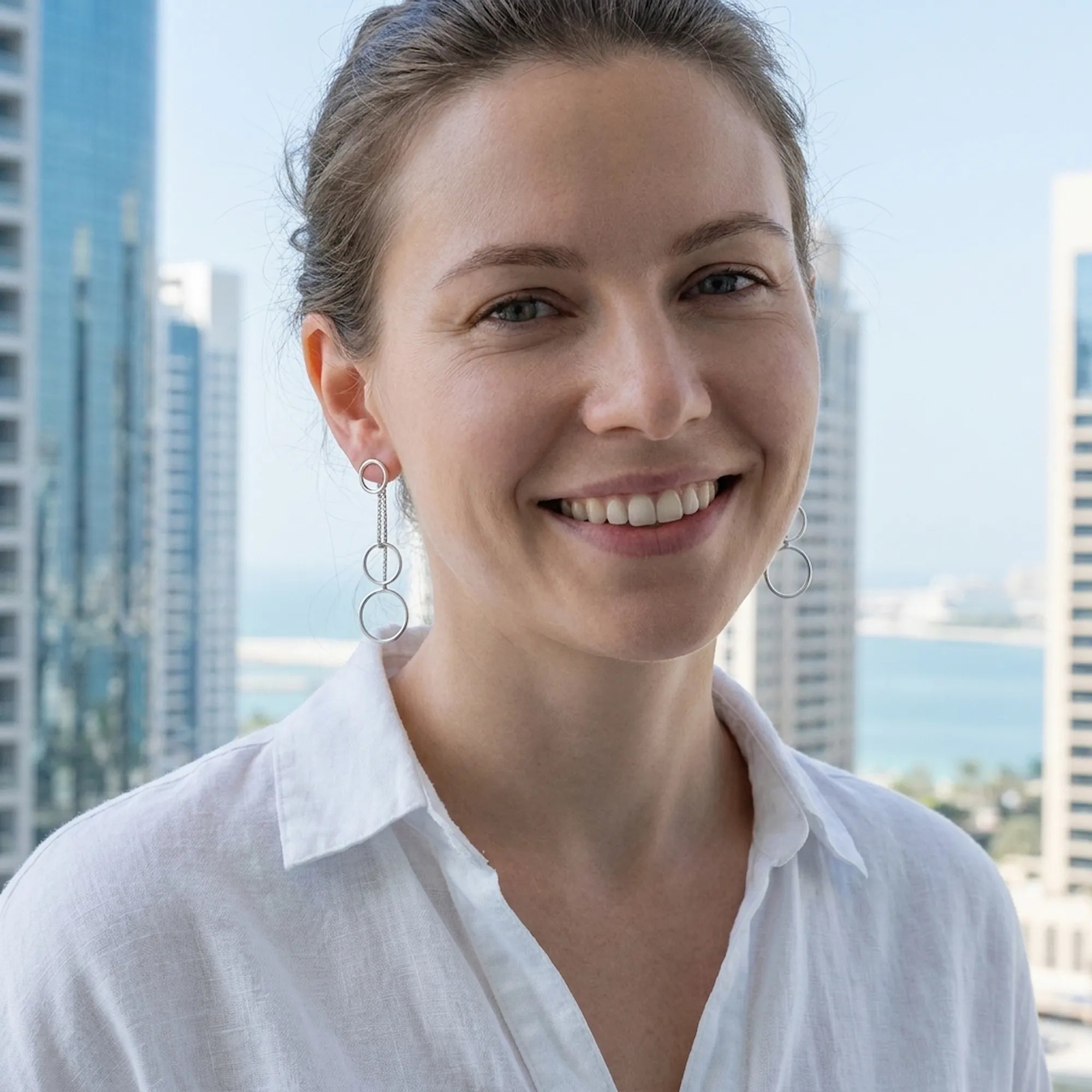  Woman wearing silver circle cascade drop earrings smiling outdoors with Dubai Marina towers and waterfront behind