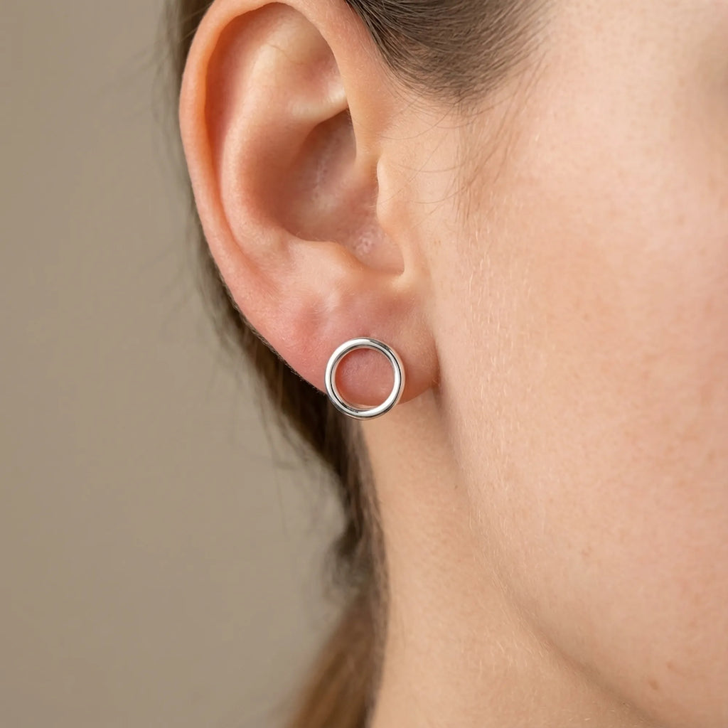 Close-up of ear wearing silver open circle stud earring in stud-only mode, neutral taupe background