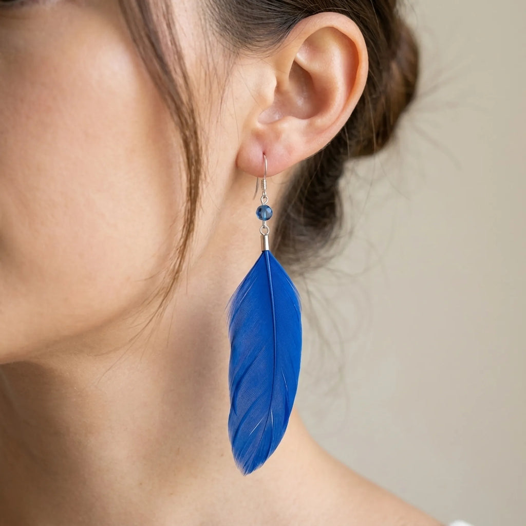 Cobalt blue feather earring worn on ear — full 8 to 10cm drop against bare neck, shepherd hook and crystal bead detail visible