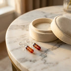 Pair of cognac amber drop earrings resting on a marble surface next to a cream velvet jewelry box for gift inspiration