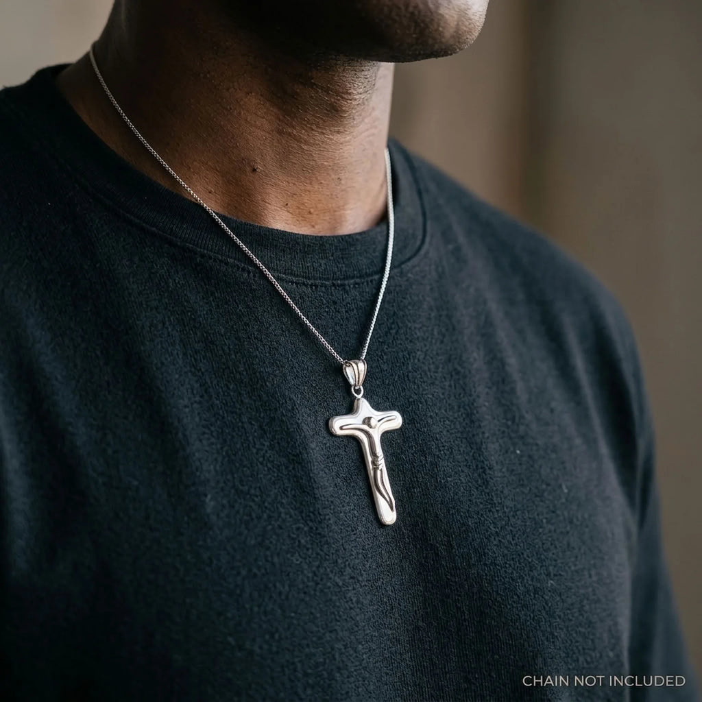 Man wearing a chunky silver crucifix pendant with abstract Christ figure, chain not included.