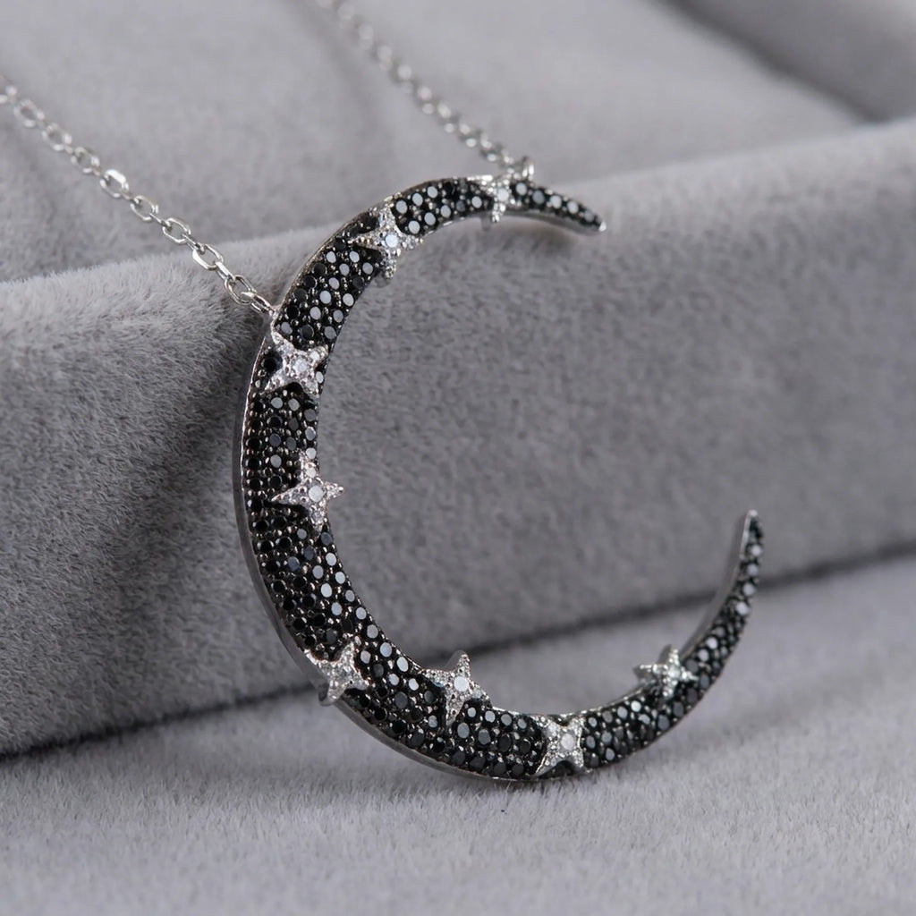 Close-up of crescent moon pendant on grey velvet — black and white zircon pavé hand-set on rhodium silver base