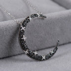 Close-up of crescent moon pendant on grey velvet — black and white zircon pavé hand-set on rhodium silver base