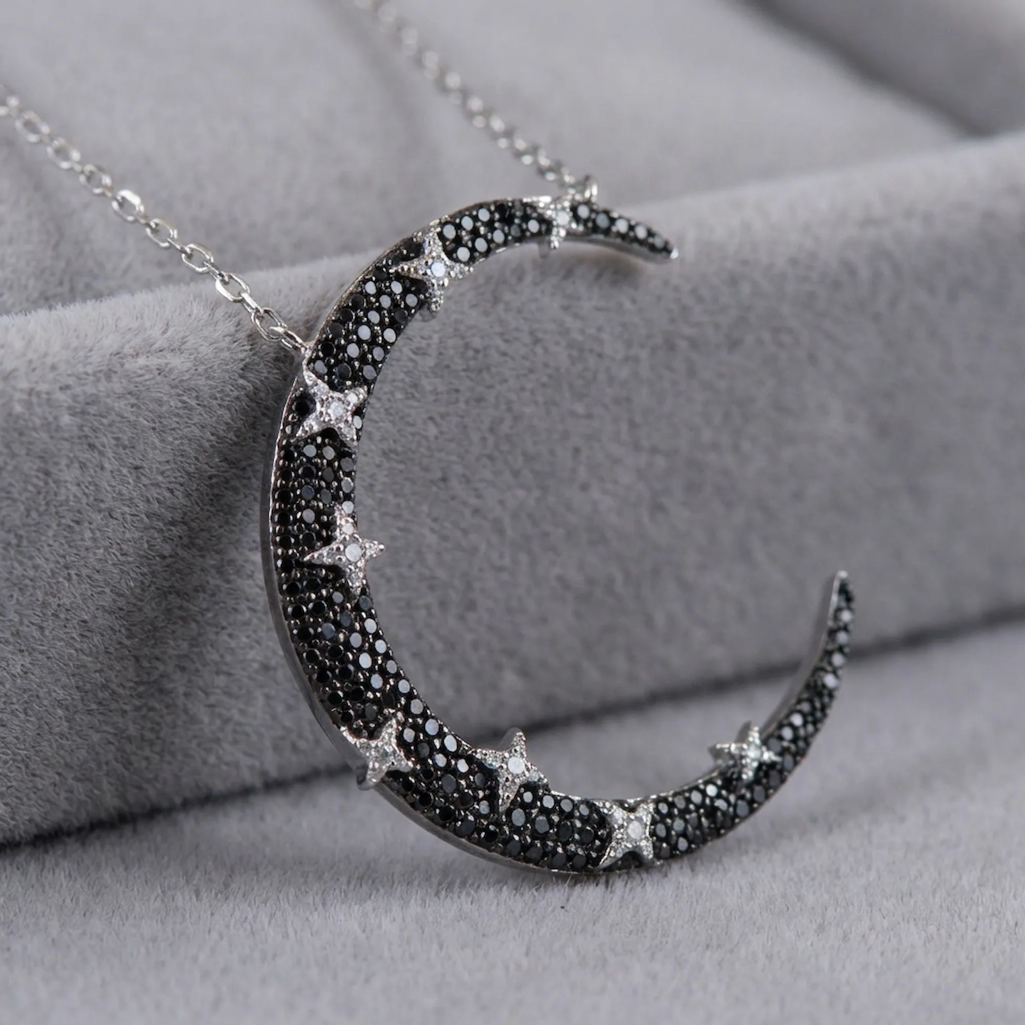 Close-up of crescent moon pendant on grey velvet — black and white zircon pavé hand-set on rhodium silver base