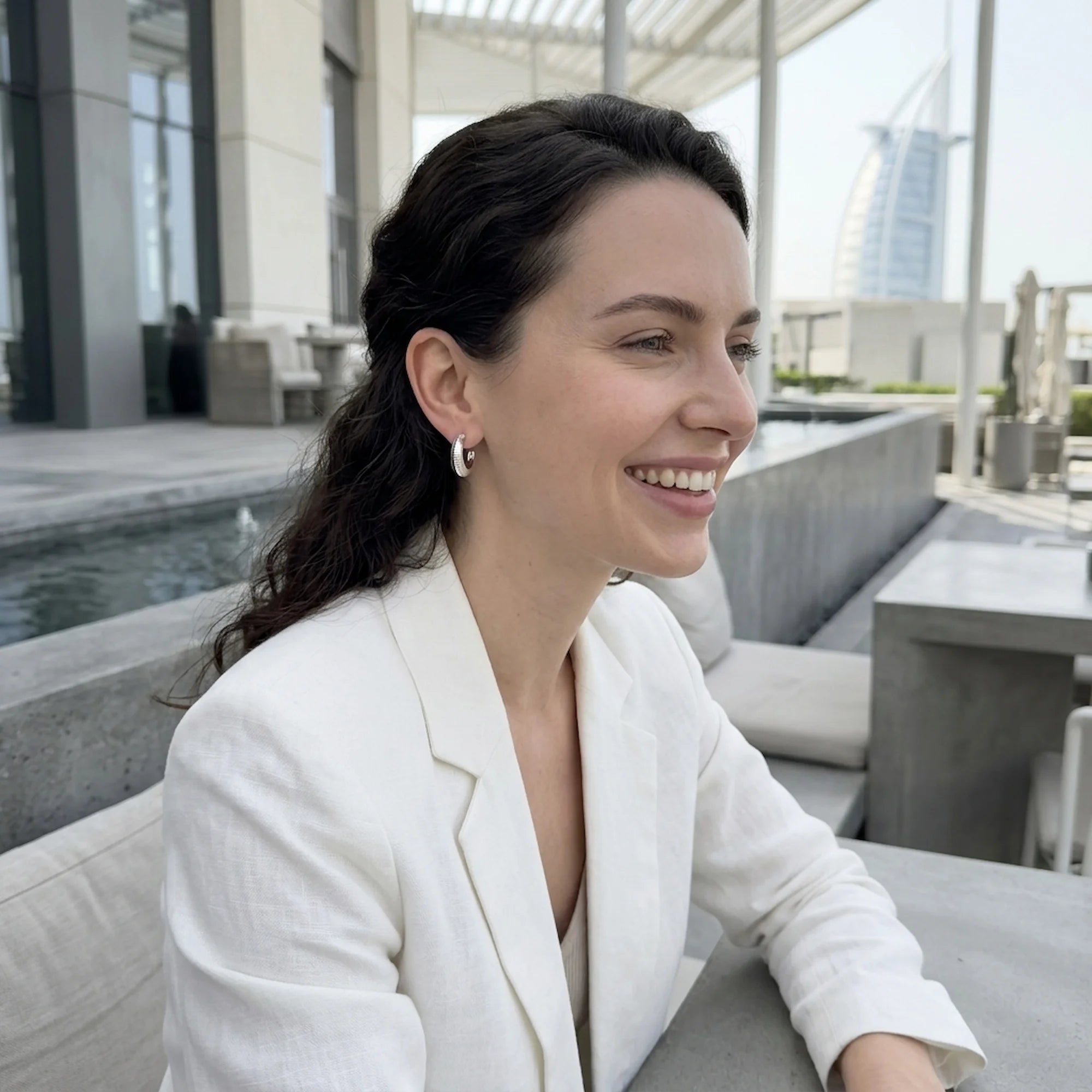 Woman wearing 925 silver crescent moon hoop earrings outdoors near the Burj Al Arab in Dubai.