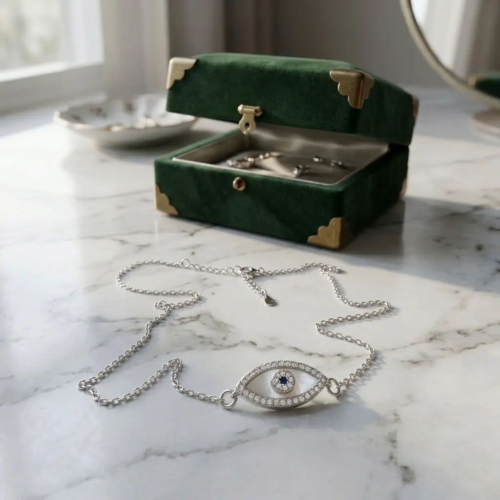 Close-up of mother of pearl evil eye necklace resting on marble next to a green velvet jewelry box.