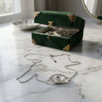 Close-up of mother of pearl evil eye necklace resting on marble next to a green velvet jewelry box.