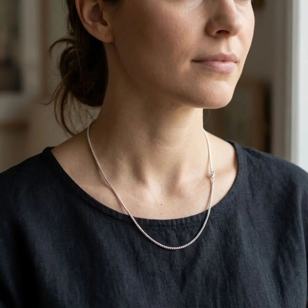Woman wearing a delicate silver-tone chain necklace with a charcoal top.