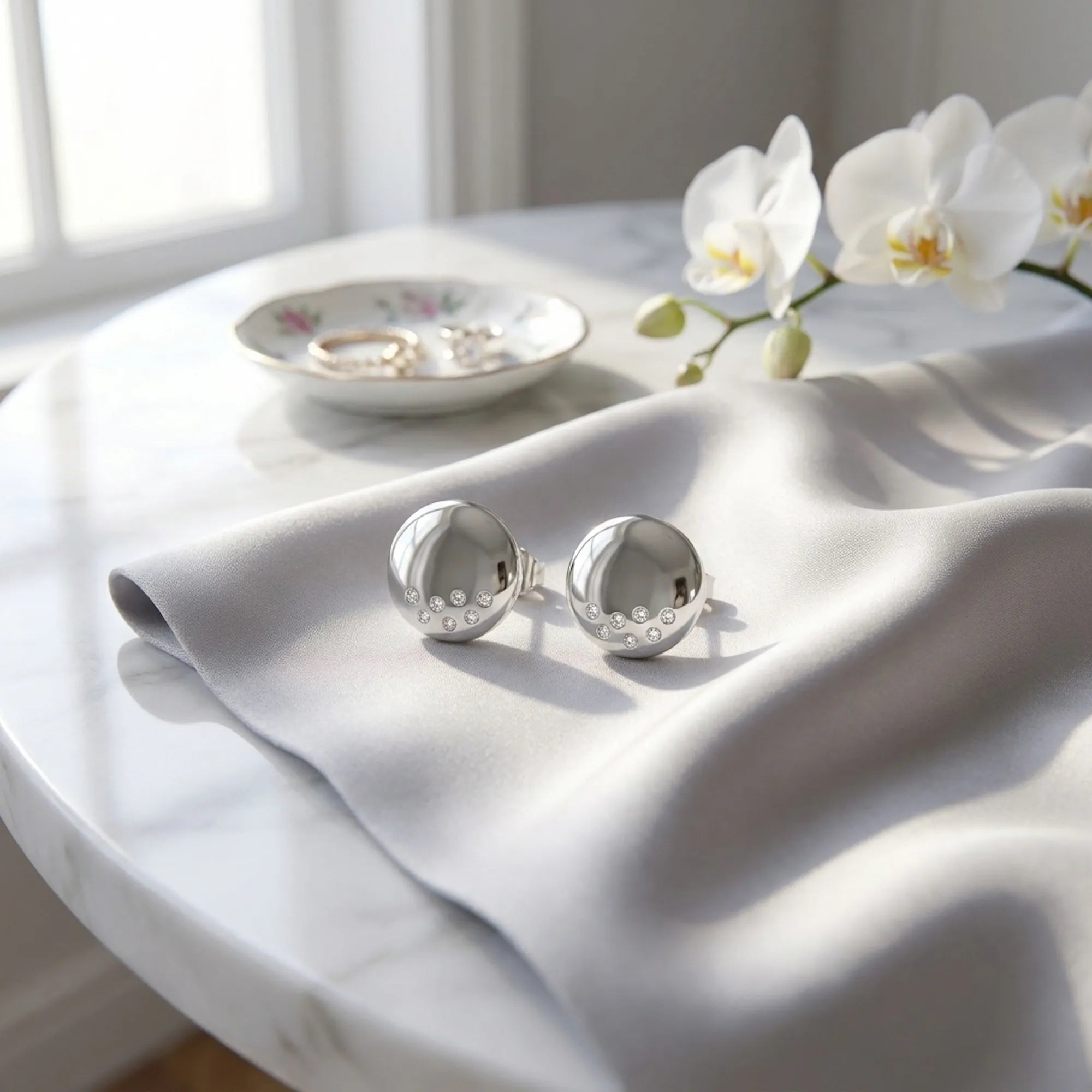 Polished silver dome stud earrings on grey satin fabric with white orchid — 925 sterling silver styled detail