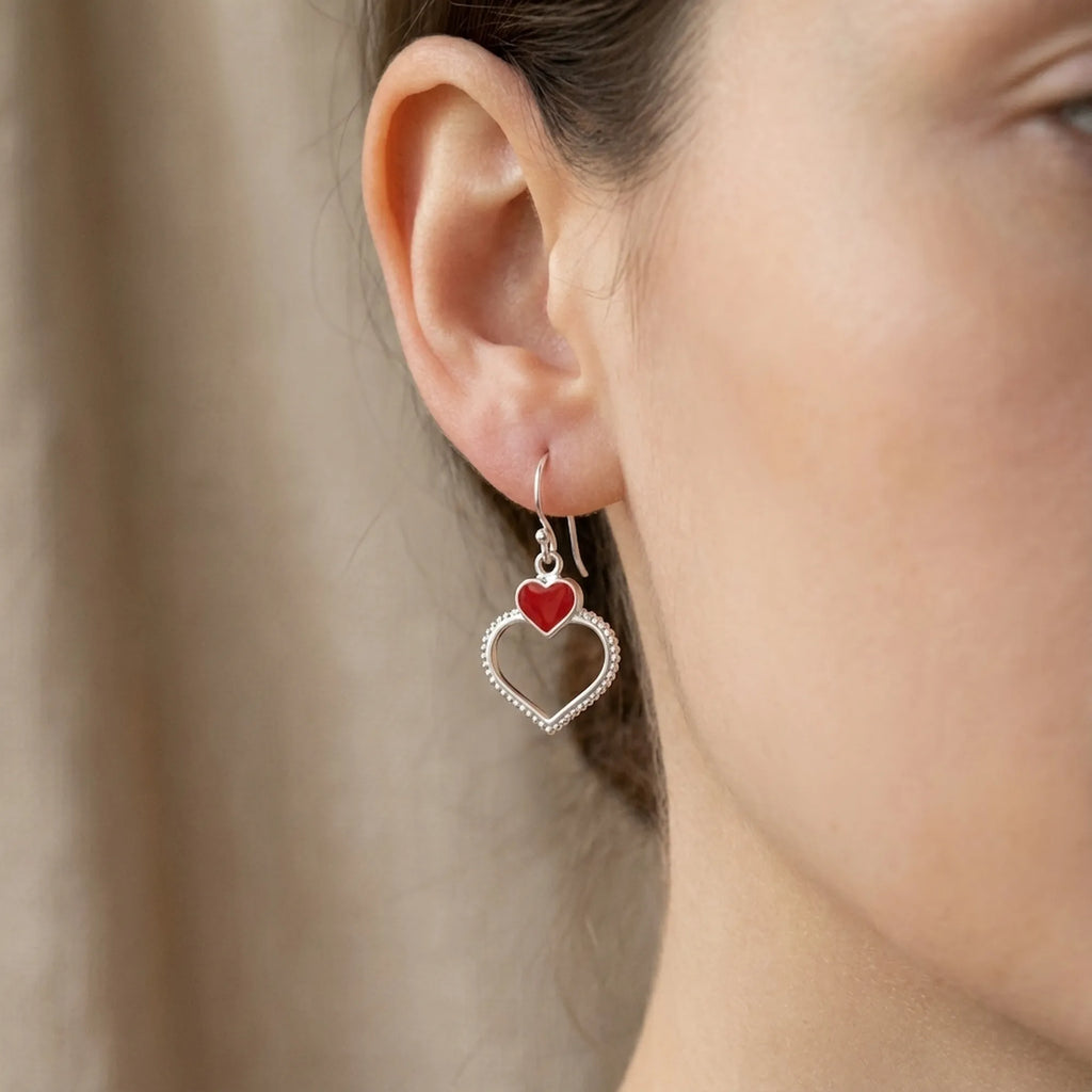 Close-up of ear wearing silver double heart drop earring showing red enamel upper heart and beaded open silver heart below