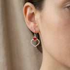 Close-up of ear wearing silver double heart drop earring showing red enamel upper heart and beaded open silver heart below