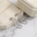 Double link silver earrings resting on a cream velvet jewelry box and white marble in Dubai.