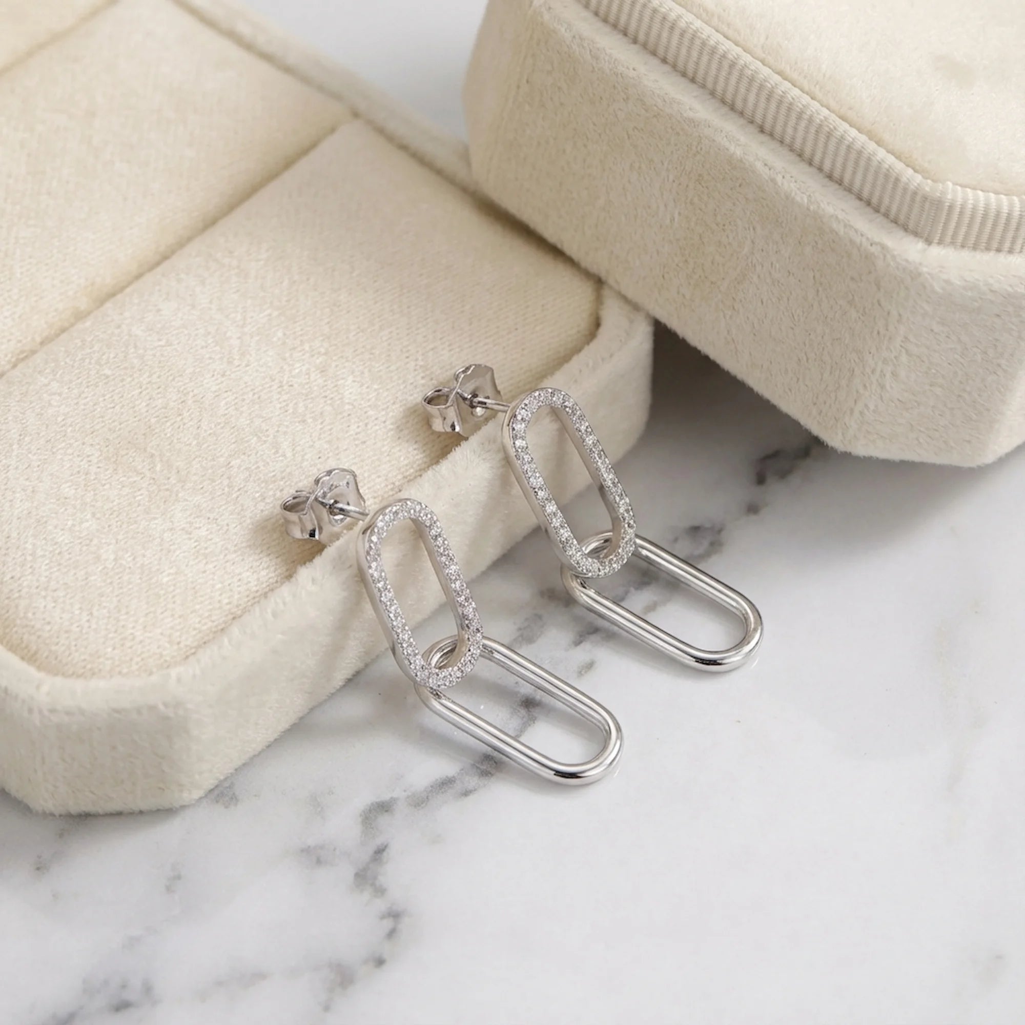 Double link silver earrings resting on a cream velvet jewelry box and white marble in Dubai.