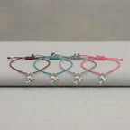 All four silver dove charm bracelets laid on grey linen showing burgundy, teal blue, lavender and rose pink cord options UAE.