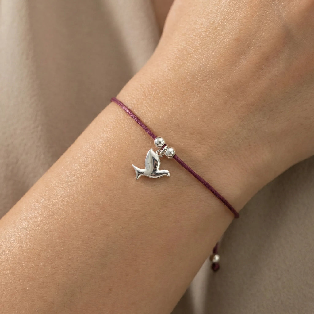 Silver dove charm bracelet on burgundy cord worn on wrist close-up showing adjustable sliding closure and dove detail