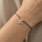 Silver dove charm bracelet on burgundy cord worn on wrist close-up showing adjustable sliding closure and dove detail