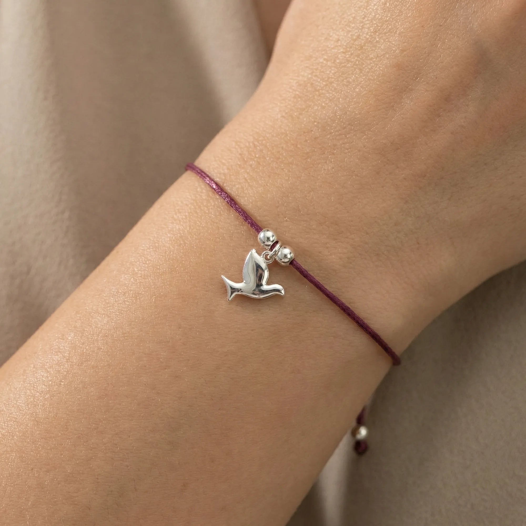 Silver dove charm bracelet on burgundy cord worn on wrist close-up showing adjustable sliding closure and dove detail