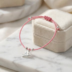 Rose pink cord silver dove charm bracelet looped around open Luna Dura cream velvet gift box on white marble