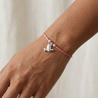 Silver dove charm bracelet on rose pink cord worn on wrist showing polished mid-flight dove charm and silver beads