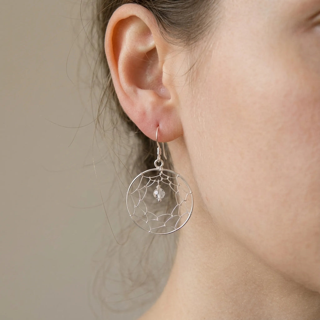 Close-up of ear wearing silver dreamcatcher drop earring showing hand-woven wire web and CZ centre bead detail