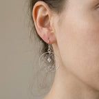 Close-up of ear wearing silver dreamcatcher drop earring showing hand-woven wire web and CZ centre bead detail