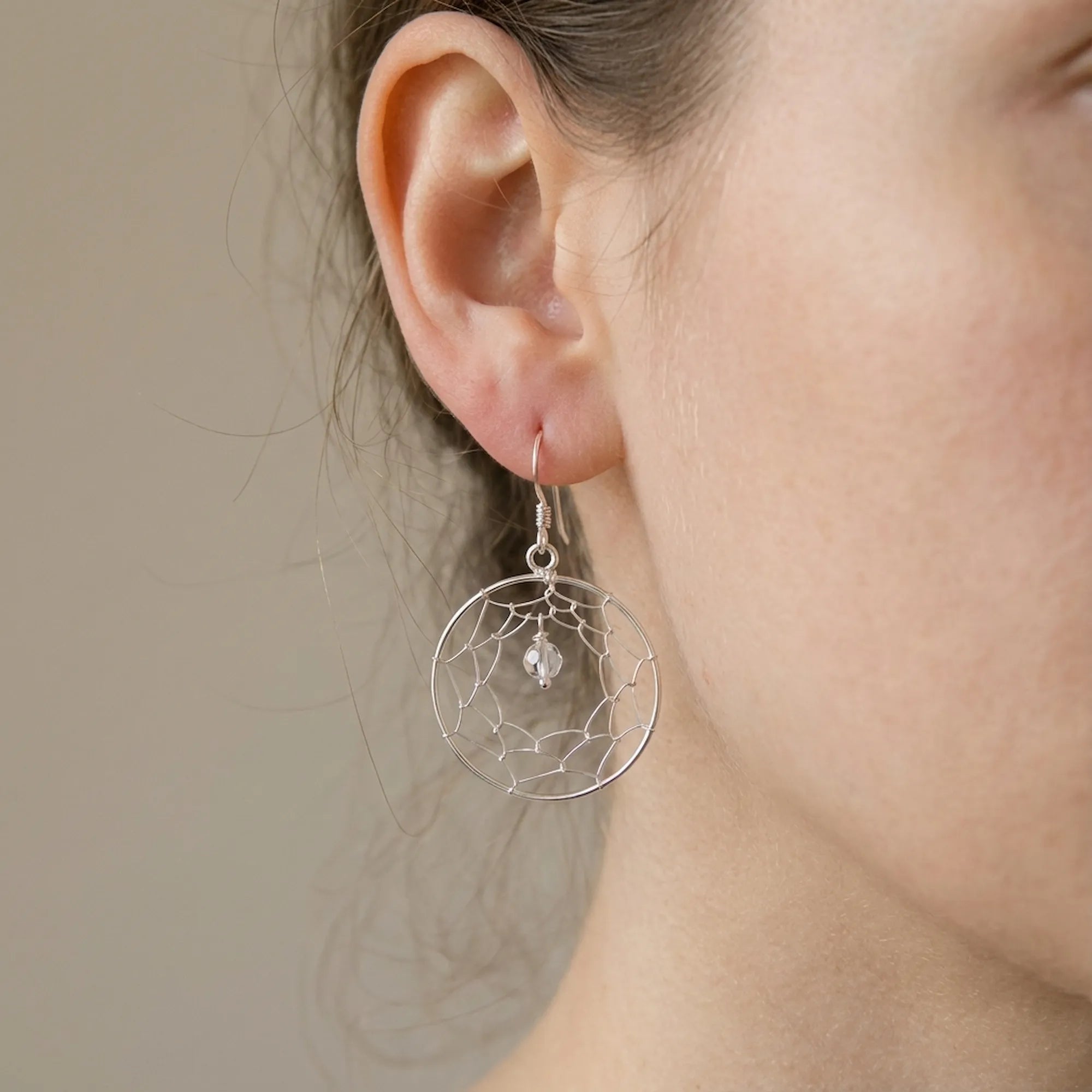 Close-up of ear wearing silver dreamcatcher drop earring showing hand-woven wire web and CZ centre bead detail