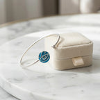 Azure blue topaz evil eye cuff bangle resting on cream jewellery box on white marble