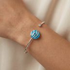 Close-up of azure blue topaz evil eye cuff bangle on wrist, white fabric background, Luna Dura